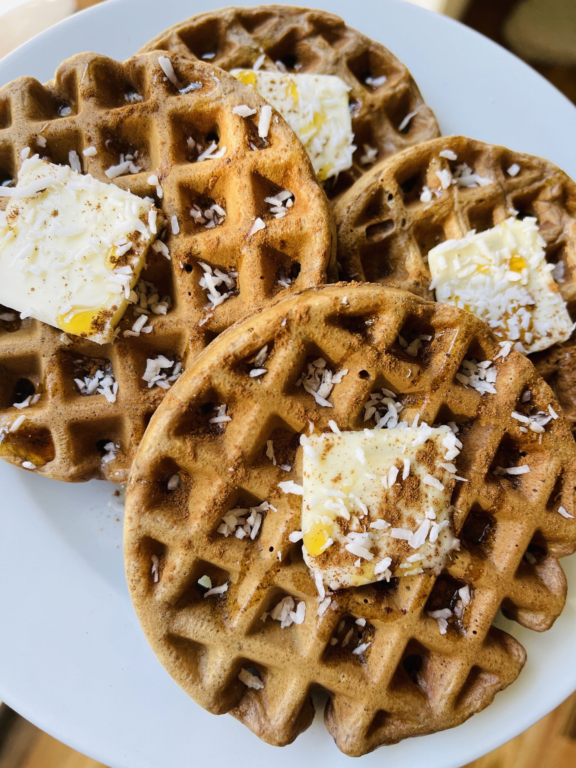 Close-up of cacao coconut date waffles with butter, maple syrup, and shredded coconut on a white plate
