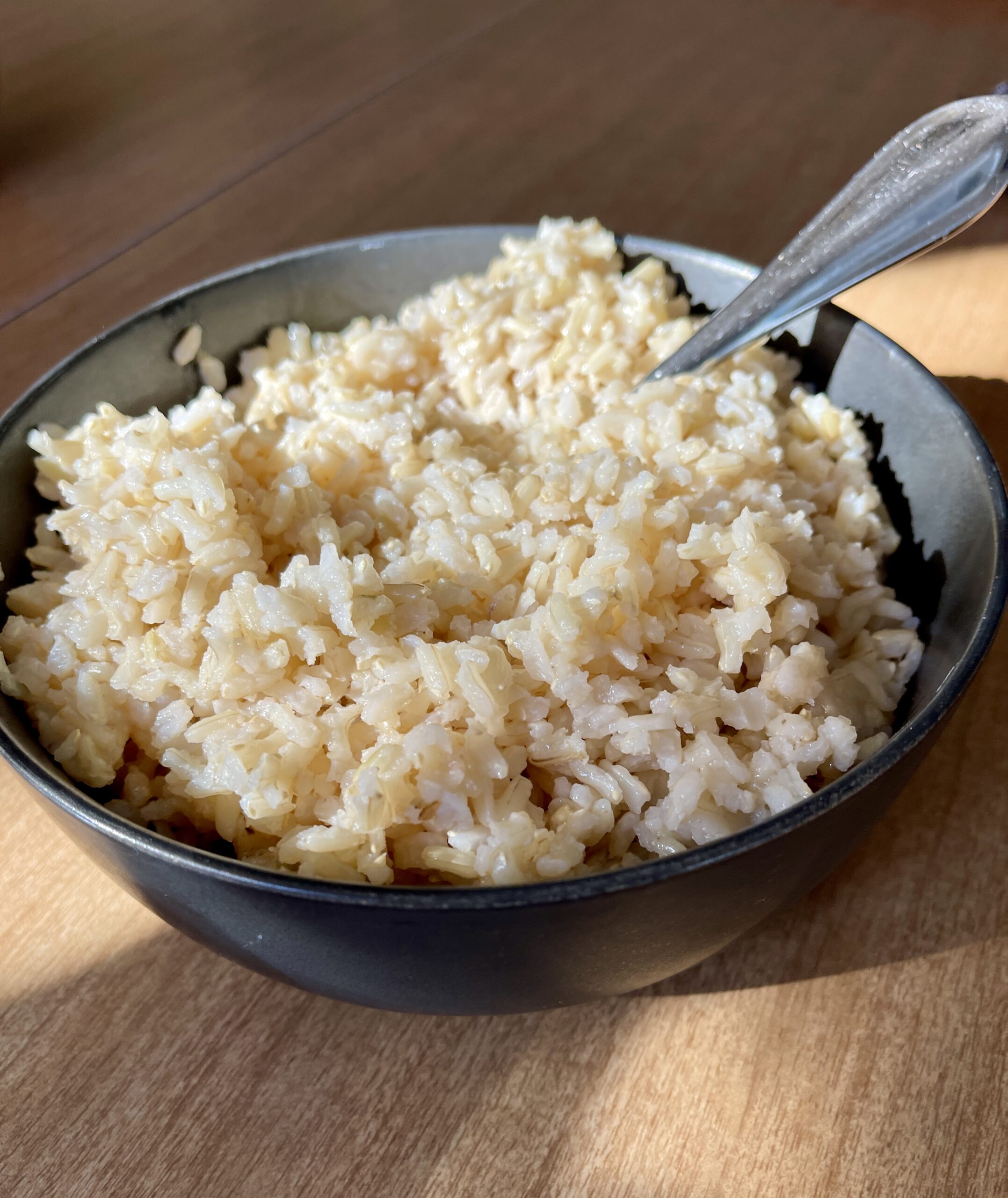 Soaked fluffy brown rice in black bowl with spoon